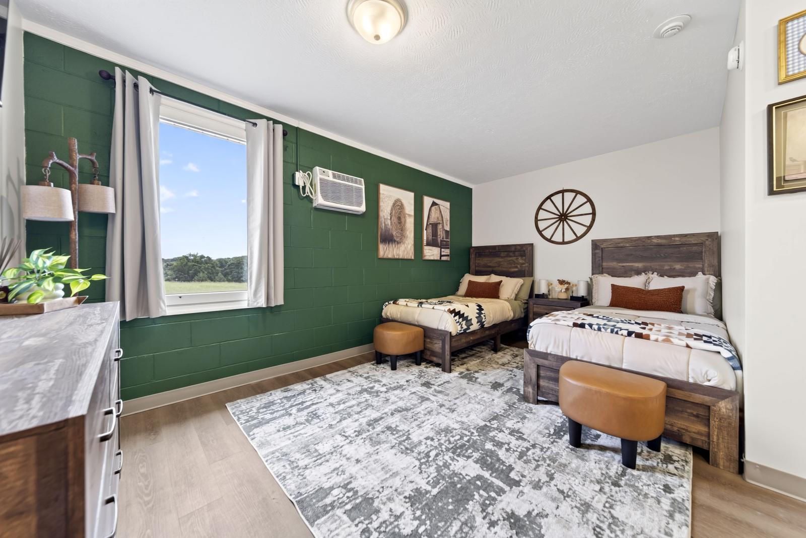 Resident bedroom with a green accent wall, two twin beds and a window onto open countryside