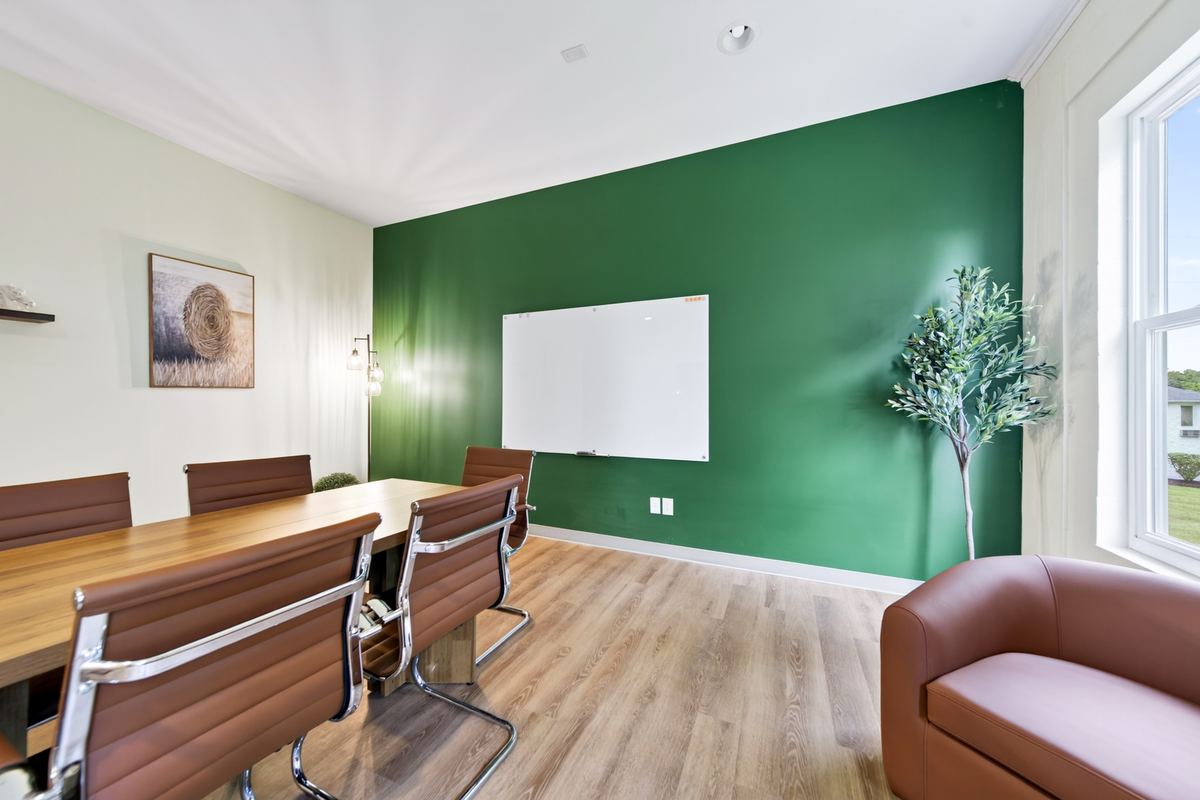 Group therapy room with a long wood table, leather chairs and a whiteboard on a deep green wall