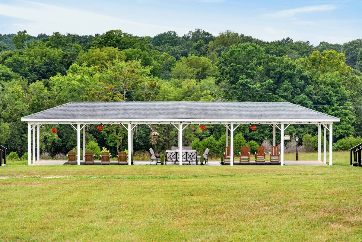 The open-air pavilion with rocking chairs and string lights, backed by woodland