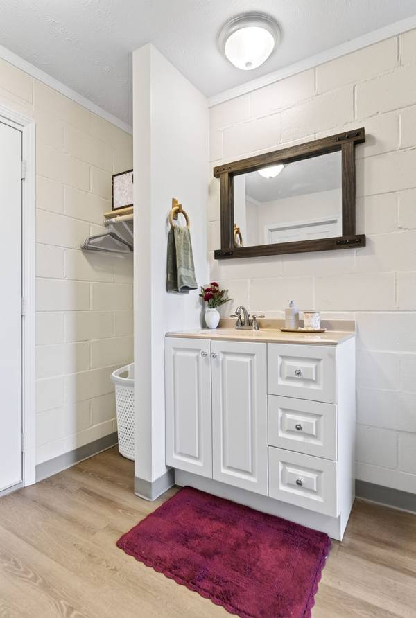 White vanity with mirror and flowers beside a hanging rail with hangers and a laundry basket