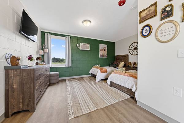 Bedroom with a wood dresser, wall-mounted TV, green accent wall and two neatly made twin beds
