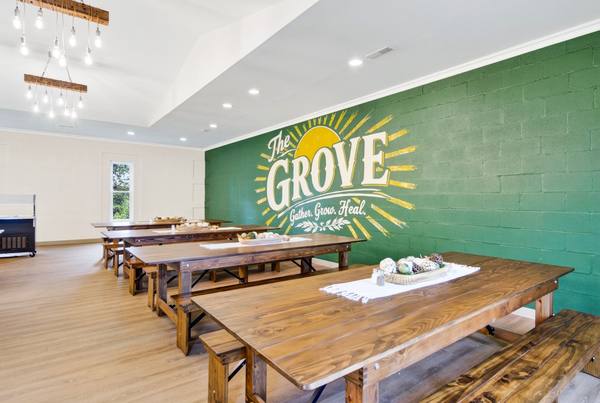 Wooden farmhouse tables and benches facing a green wall painted with the Grove sunrise mural