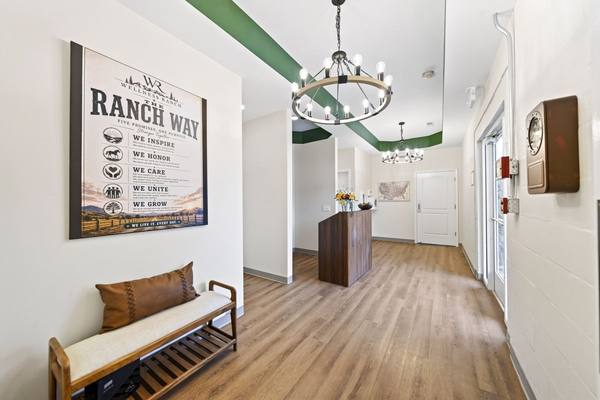 Entry hallway with a large Ranch Way poster, cushioned bench and two chandeliers leading to the desk