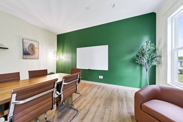 Group room with a long wood table, brown leather chairs and a whiteboard on a deep green wall