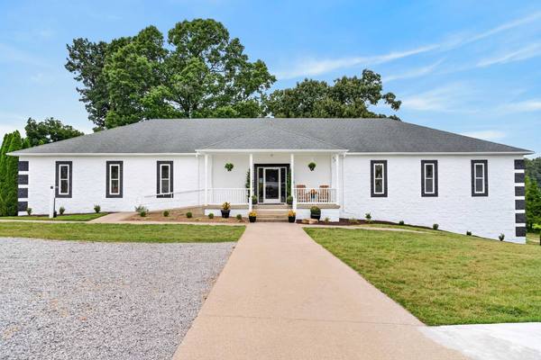 Long single-story white building with a gray roof and a concrete walkway leading to the front porch