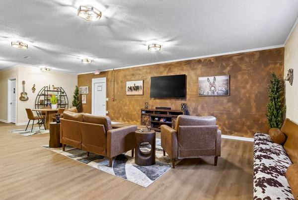 Leather sofas and armchairs in a lounge with a copper-toned brick wall, TV, and cafe table with a guitar