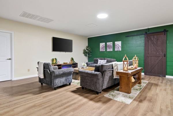 Lounge with grey armchairs facing a TV and electric fireplace, green brick accent wall and sliding barn door