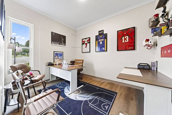 Small office with framed sports jerseys on the wall, a desk and brown leather guest chairs