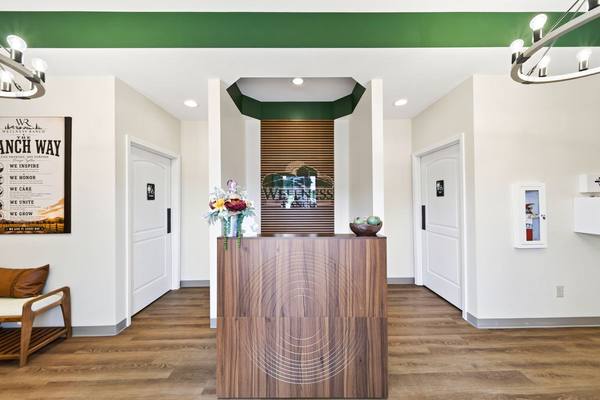 Wood reception desk facing the entry, backed by a slatted wall with the Wellness Ranch logo in glass