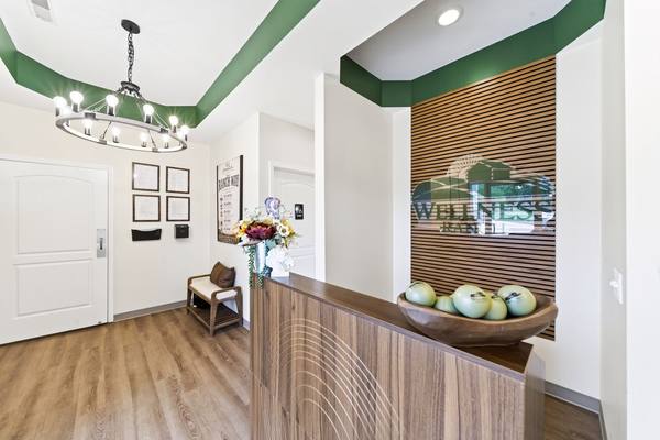 Lobby with a ring chandelier, green tray ceiling, wood reception desk and the Wellness Ranch logo wall