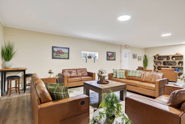 Tan leather sofas with green plaid cushions around a wood coffee table, framed farm paintings on cream walls