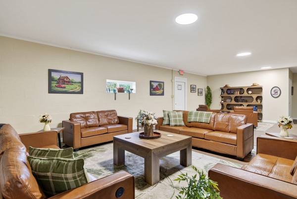 Living room with tan leather sofas and armchairs around a low wood table, bookshelf at the far end