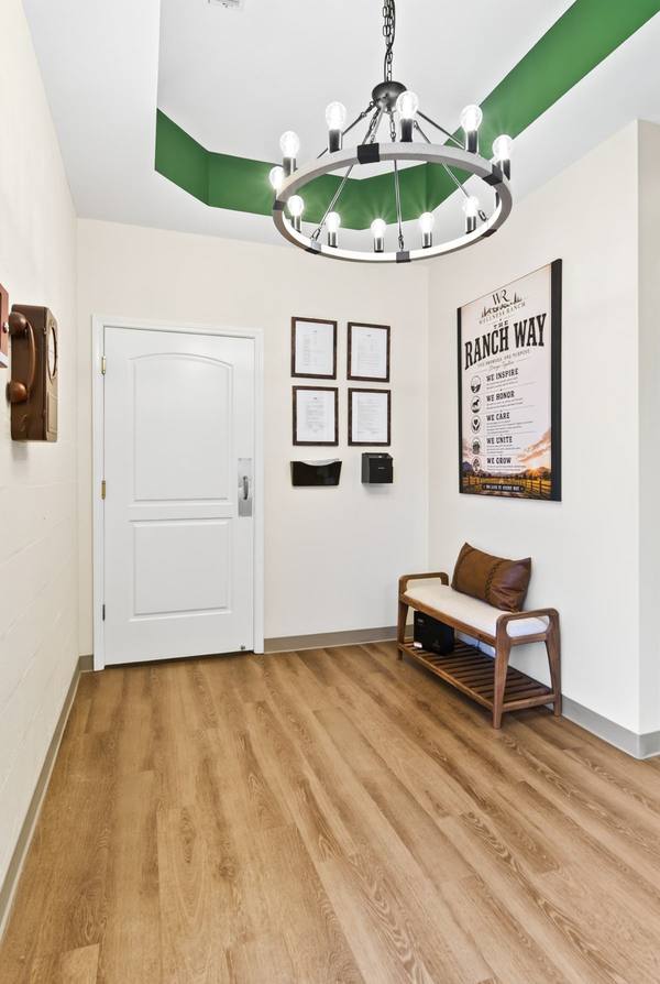 Entry corner with a wooden bench, leather pillow, framed licenses and a ring chandelier overhead