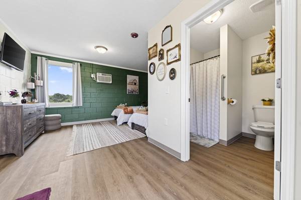 Bedroom with two twin beds against a green block wall and an open door to a private shower and toilet
