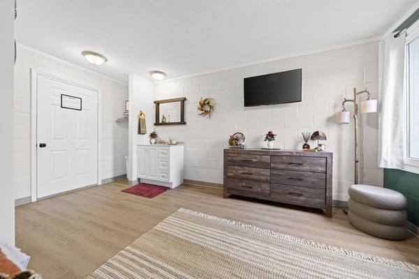 Bedroom with a wood dresser, wall-mounted TV, white sink vanity and a woven rug on light wood floor