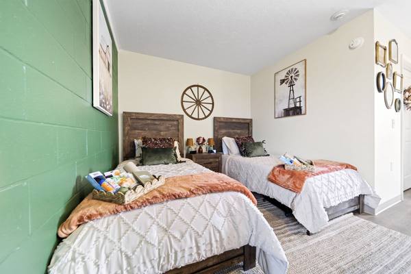 Twin beds with welcome baskets, framed windmill art and a cluster of small frames near the door