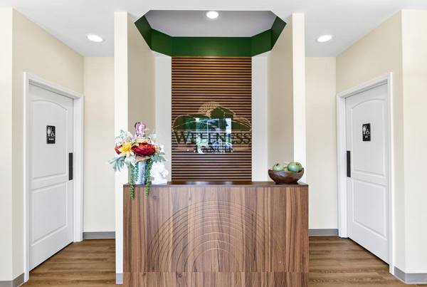 Wood reception desk beneath the Wellness Ranch logo on a slatted wood wall, with flowers and a bowl of apples