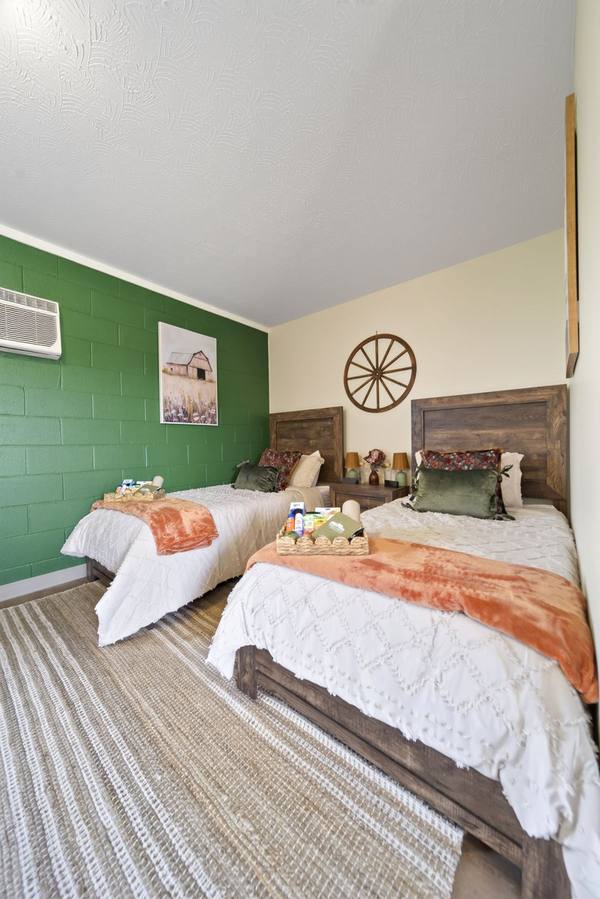Shared bedroom with two twin beds, orange throws, welcome baskets and a green accent wall