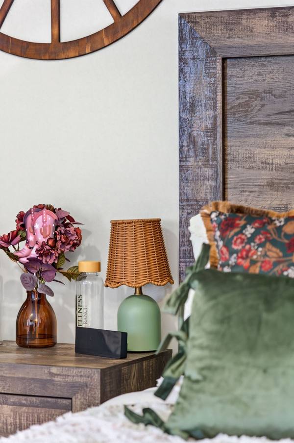 Nightstand with a rattan lamp, dried flowers in an amber vase and a Wellness Ranch water bottle