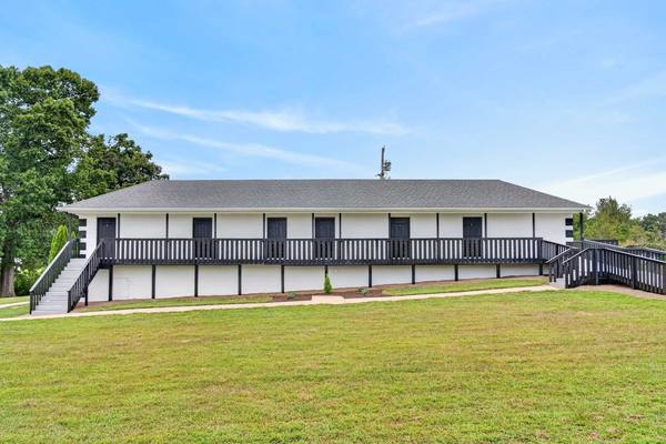 Long white residence building with a dark railed porch running its length and steps down to the lawn