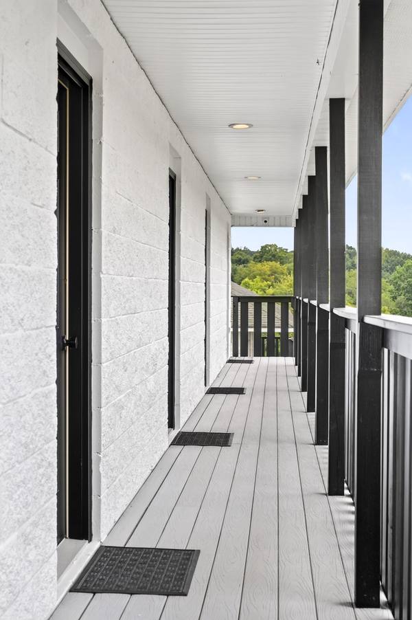 Long covered porch with white decking, black posts and railings, looking out to green wooded hills