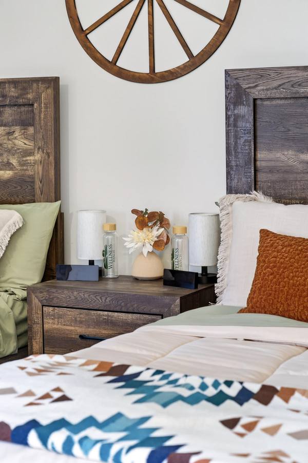 Bedside table between two beds with lamps, Wellness Ranch water bottles and a small vase of flowers