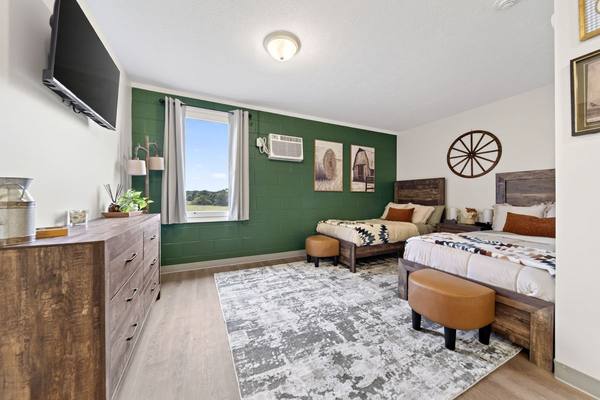 Bedroom with a green accent wall, two beds, a dresser, wall TV, and a window onto open pasture