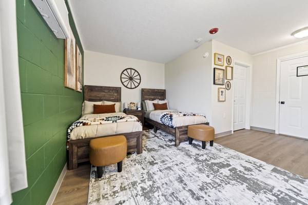 Two twin beds with patterned quilts against a green accent wall, leather ottomans, and framed prints