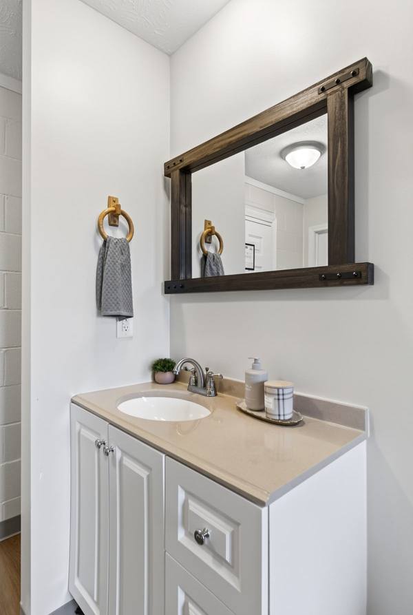 White vanity with cream countertop, wood-framed mirror, grey hand towel on a ring, and hand soap