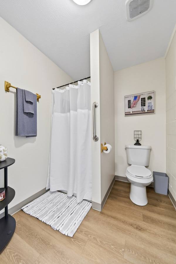 Curtained shower with a grab bar and folded towels beside a toilet in a bright resident bathroom