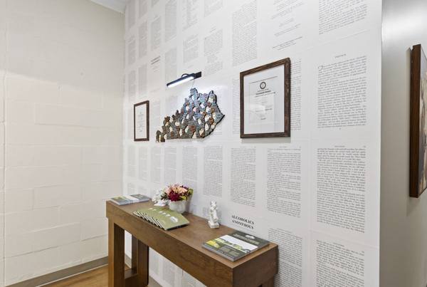 Corner wall papered with book pages, a wooden Kentucky county map, framed licenses, and a console table