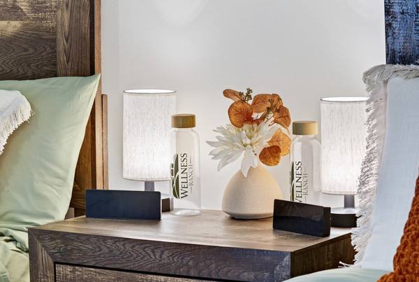 Nightstand between two beds with lamps, a vase of flowers, and Wellness Ranch water bottles