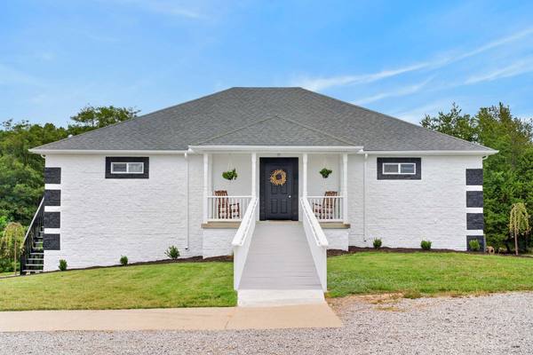 Smaller white house with a black front door, wreath, twin rocking chairs and a long white entry ramp