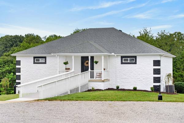 Small white house with a covered front porch, wreath on the door and a long railed ramp