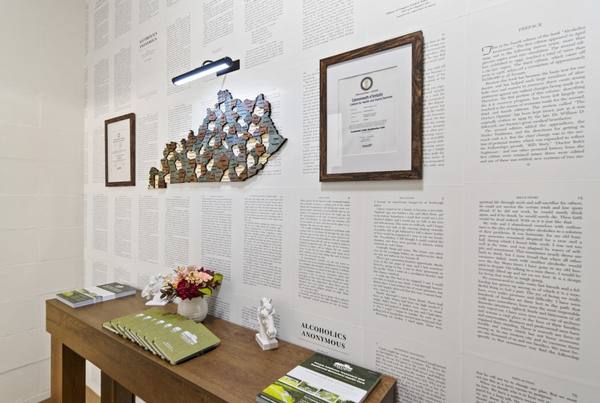 Console table with green welcome folders and flowers below a Kentucky map on a wall of printed book pages