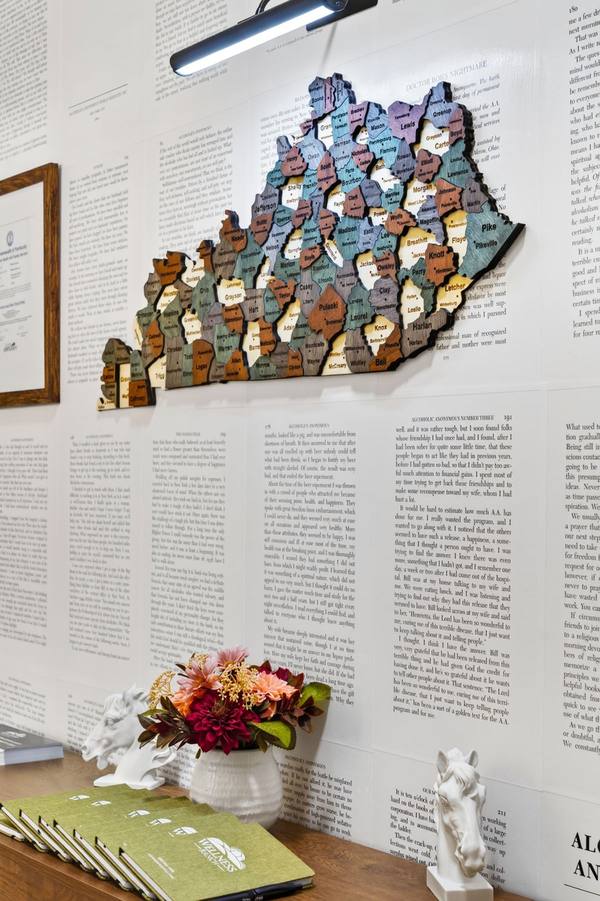Carved wooden map of Kentucky with every county labeled, above a table of flowers and green booklets