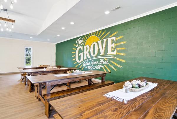 Dining hall with wooden tables and benches beside a green wall mural reading The Grove, Gather Grow Heal