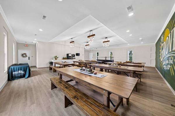 Dining hall lined with long wooden tables and benches under hanging Edison-bulb light fixtures