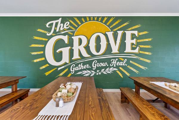 Dining hall with long wooden farm tables and benches in front of The Grove mural