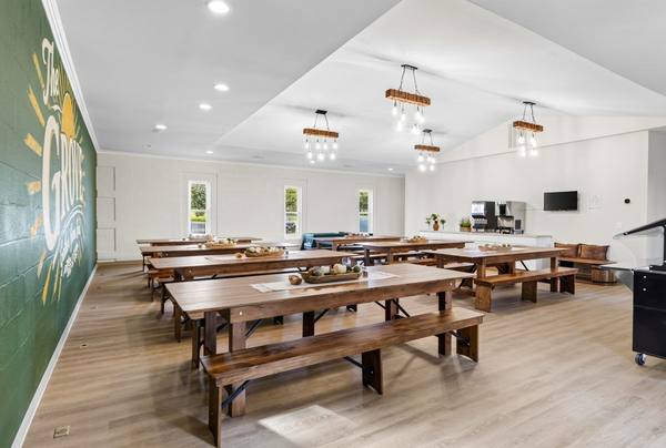 Dining hall with long wooden farmhouse tables and benches beneath a painted "The Grove" mural