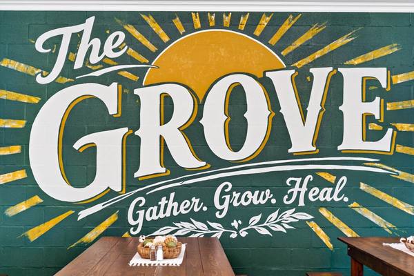 Hand-painted mural reading The Grove, Gather. Grow. Heal., in green and gold above a wooden table