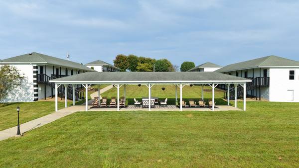 White open-sided pavilion with rocking chairs on the lawn between two residence buildings