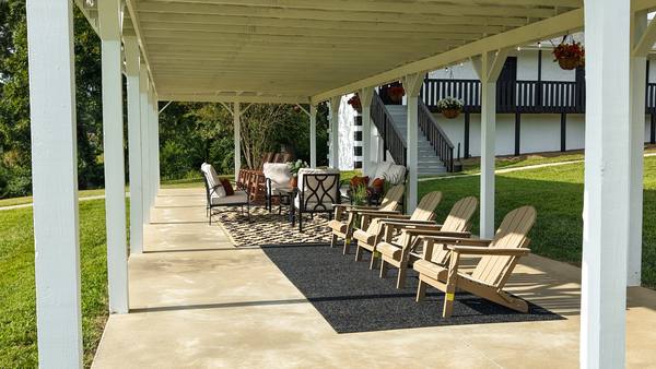 View along the covered pavilion with Adirondack chairs, outdoor rugs and hanging baskets