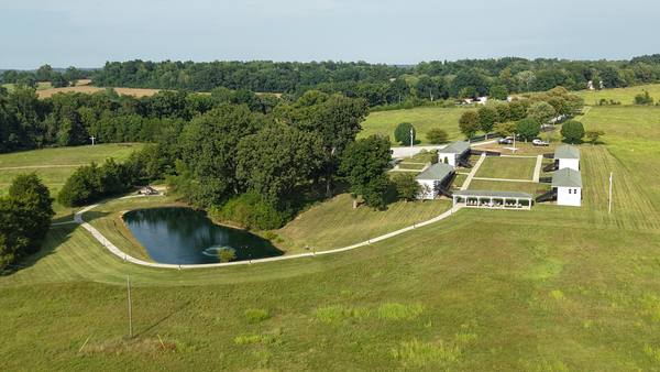 Aerial across rolling fields showing the pond in the foreground and the ranch buildings beyond
