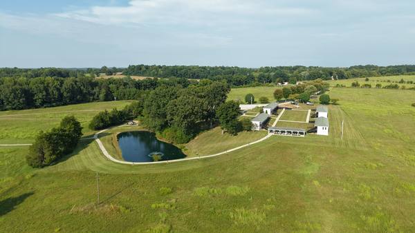 High aerial of the full property: pond, mown fields, the gravel drive and the ranch buildings