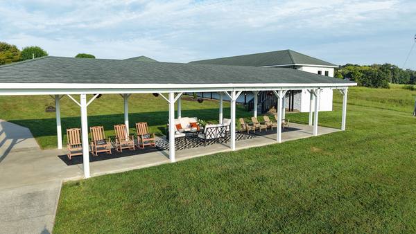 Open pavilion with rocking chairs and cushioned sofas on the lawn with the residence behind