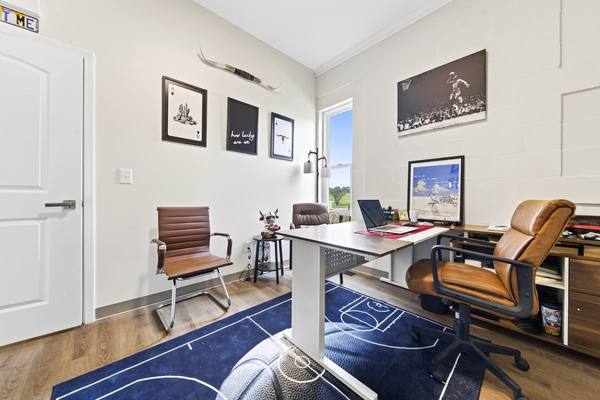 Office corner with a desk, leather chairs and a navy basketball court rug on wood floors
