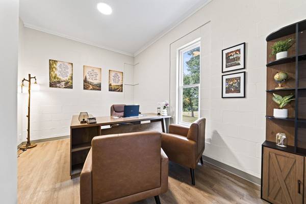 Office with a desk, laptop and two brown leather armchairs beside a sunny window