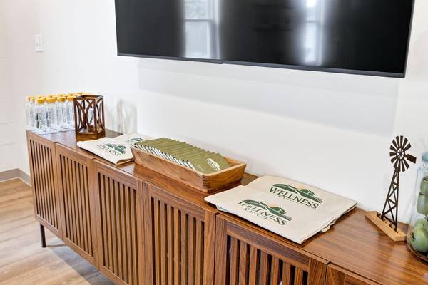Wooden console with bottled water, Wellness Ranch tote bags and brochures below a wall-mounted TV