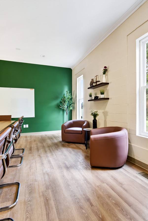 Therapy room with green accent wall, whiteboard, counter seating and two leather armchairs by a window